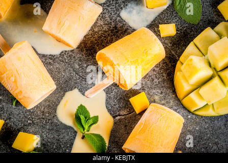 Ice cream, popsicles. Organic dietary foods, desserts. Frozen mango smoothie, with mint leaves and fresh mango fruit, on black stone table. Copy space Stock Photo