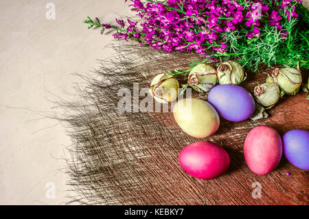 Brightly colored Easter eggs near the bouquet of wild flowers and dried buds of roses on a underlay of straw Stock Photo