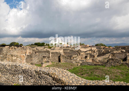 View of the walls of homes in Pompeii, with small white church in the background. Stock Photo