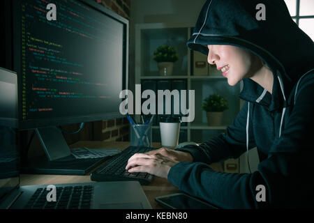 happy young female hacker using computer crimes and typing virus program code to steal personal information through online system. Stock Photo
