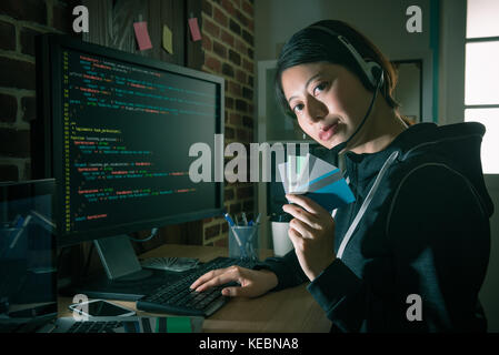 beautiful young female hacker using code stealing credit card information and wearing headset preparing making telemarketing to get money. Stock Photo