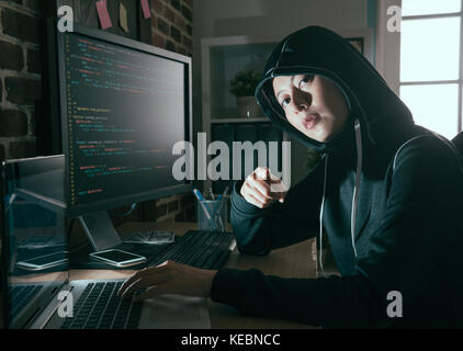 young female computer programmer as hacker doing illegal working online and looking at camera pointing showing threat concept. Stock Photo