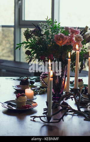 The beautiful festive table with rustic bouquet, dessert and candles Stock Photo