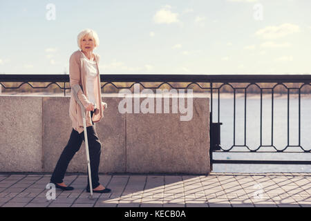 Elderly woman walking along the bridge on crutches Stock Photo