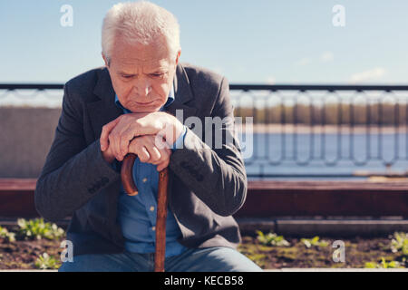 Upset senior man pondering while sitting on bench Stock Photo