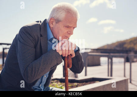 Sorrowful elderly man sitting on the bridge Stock Photo