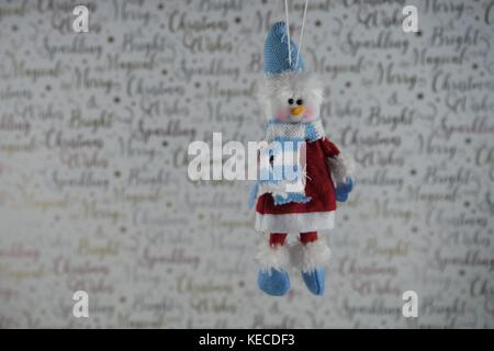 red white Christmas photography picture of hanging up Christmas decoration of cute snowman in hat scarf with xmas wrapping paper background Stock Photo