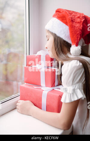 nice little girl in santa hat dreaming by the window hugging christmas gifts stock photo - Nice Christmas Gifts nice little girl in santa hat dreaming by the window hugging christmas gifts stock photo - Nice Christmas Gifts