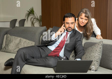 arab man working at home while woman is looking over his shoulder trying to get his attention Stock Photo