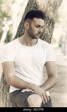 Sad and thoughtful man leaning against the trunk of a tree. Stock Photo