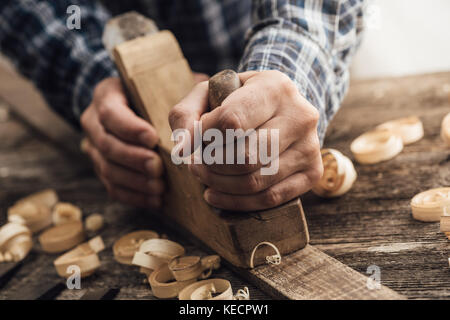 Carpenter working in his workshop, he is smoothing a wooden board using a planer, carpentry, carpentry, woodworking and craftsmanship concept Stock Photo