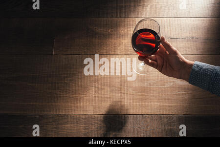 Man holding a balloon glass of delicious red wine on a rustic wooden table: wine tasting and celebration concept