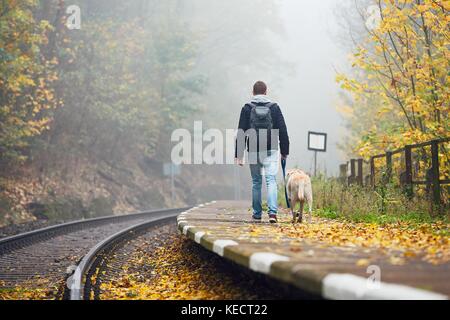 Old railway station in fog. Autumn mood on the trip. Young man traveling with his dog by train. Stock Photo