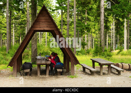 Wooden tourist shelter on hiking trail rest area in spruce forest with female hiker taking rest inside. The Owl Mountains Landscape Park, south Poland Stock Photo