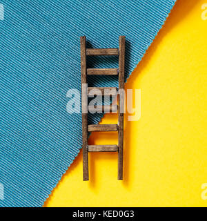 Wooden ladder on yellow and blue background Stock Photo