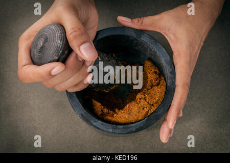 The Women hold pestle with mortar and and spice red curry paste ingredient of thai popular food on dark concrete background. Stock Photo