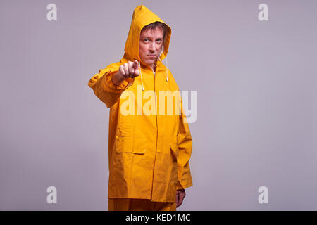 A serious middle aged man standing in a yellow raincoat and pointing in to the camera Stock Photo