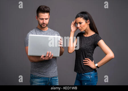 A handsome young man holding a laptop next to his girlfriend who is feeling upset Stock Photo