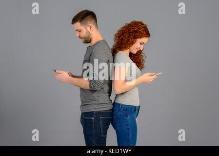 A beautiful young couple standing back to back while holding and using their smartphones Stock Photo
