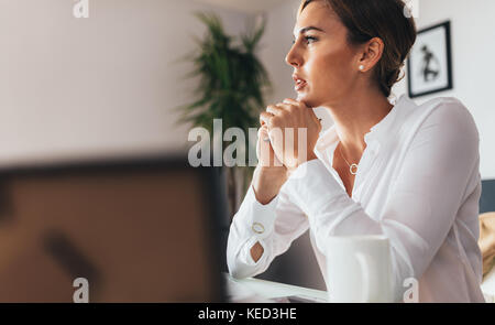 Woman sitting at her desk in office thinking deeply. business woman sitting in office with chin resting on hands looking away. Stock Photo