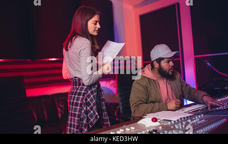 Female singer with man working on audio mixing console in recording studio. People working in professional music studio. Stock Photo