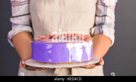 Pastre shef making mousse cake with purple mirror glaze and decorated with chocolate pink flowers. Stock Photo