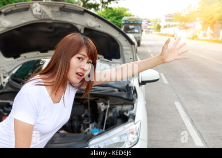 Woman looking for help after a car breakdown, standing besides car and hitching a ride. Stock Photo