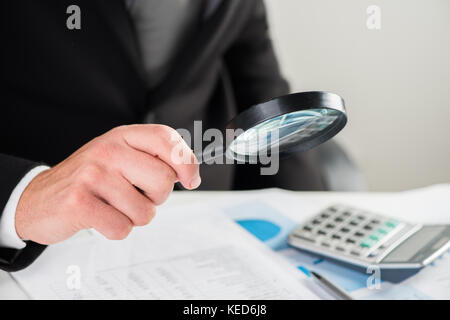 Businessman looking through a magnifying glass to documents Stock Photo