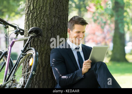 Smiling Young Male Businessman Using Digital Tablet In Park Stock Photo