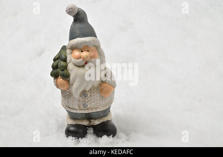 ceramic figure of Father Christmas with gray clothes and Christmas tree on snwo background, horizontal Stock Photo