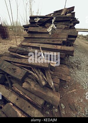 Terrible smell pile of extracted old wooden ties. Old oiled used oak railway sleepers stored after big reconstruction of old railway station. Stock Photo