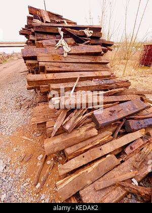 Terrible smell pile of extracted old wooden ties. Old oiled used oak railway sleepers stored after big reconstruction of old railway station. Stock Photo