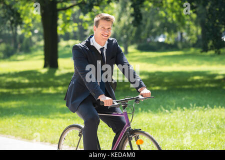 Happy Young Male Businessman Riding Bicycle In Park Stock Photo