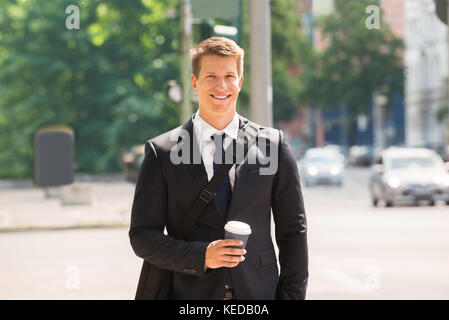 Smiling Young Man Walking On Street Holding Coffee Cup Stock Photo