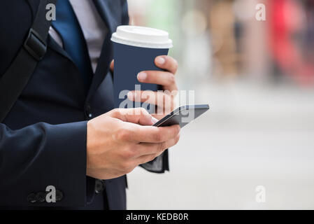 Close-up Of A Businessperson Hand With Coffee Cup And Mobile Phone Stock Photo