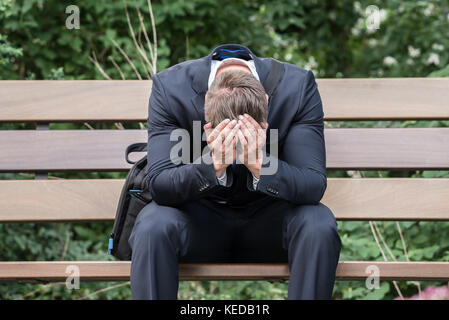 Sad Young Businessman Sitting On Bench Suffering From Headache Stock Photo