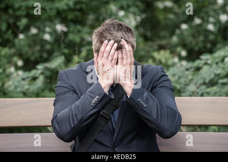 Sad Young Businessman Sitting On Bench Suffering From Headache Stock Photo