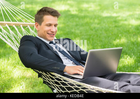 Happy Young Man Lying In Hammock Using Laptop Stock Photo