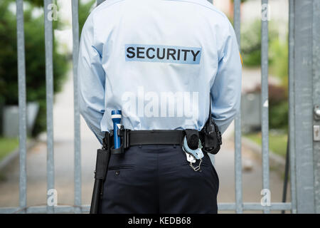 Rear View Of A Security Guard Standing In Front Of Gate Stock Photo