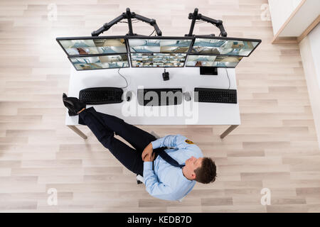 High Angle View Of Security Guard Sleeping In Front Of Multiple Computers Showing CCTV Footage Stock Photo