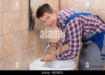 Young Male Plumber Hand Fixing Tap Of Sink In Bathroom Stock Photo