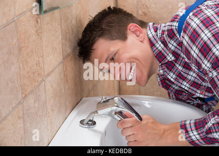 Young Male Plumber Hand Fixing Tap Of Sink In Bathroom Stock Photo