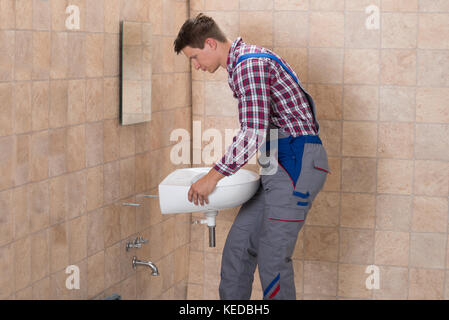 Side View Of Happy Male Plumber Installing Sink In Bathroom Stock Photo