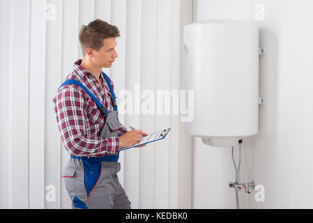 Young Male Plumber Holding Clipboard Checking Electric Boiler Stock Photo