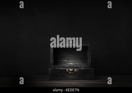 A dark wooden treasure chest with lid open and lit on planked surface with black chalkboard background. Stock Photo