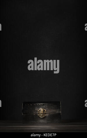 A dark wooden treasure chest with closed lid and metal clasp on planked surface with black chalkboard background. Stock Photo