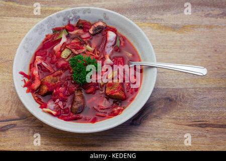 Borscht soup in tan bow, garnished with parsley leaves, on wooden table . Borscht is a traditional Ukrainian soup combining meat, beetroots and other  Stock Photo