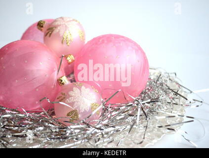 Frosted pink Christmas balls and baubles on a nest of silver hair in a mother-of-pear plate with copy space Stock Photo