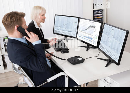 Two Businesspeople Analyzing Stock Charts On Multiple Computer Screens Stock Photo