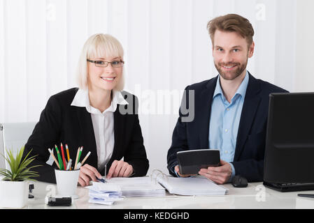 Two Young Businesspeople Calculating Bills At Desk In Office Stock Photo